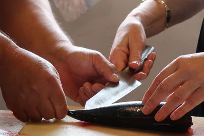 Cropped hands of people cutting fish on table