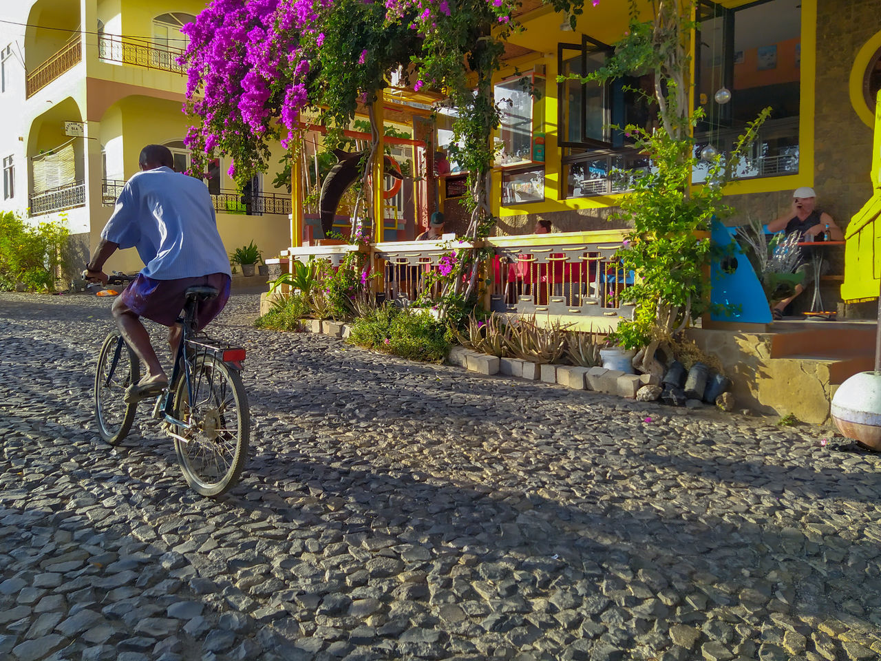 REAR VIEW OF MAN RIDING BICYCLE ON ROAD IN CITY