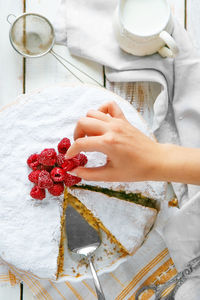 Cropped hand of woman arranging raspberries on sponge cake