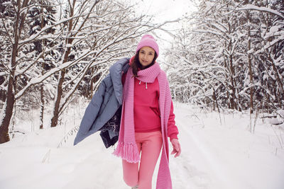 Woman enjoy in pink clothes a jacket a knitted scarf and a hat stands in a snowy forest in winter