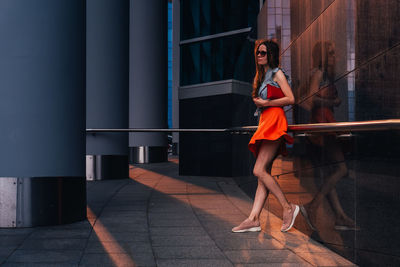 Woman looking away while standing against building in city
