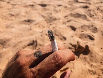 Cropped hand holding cigarette over sand