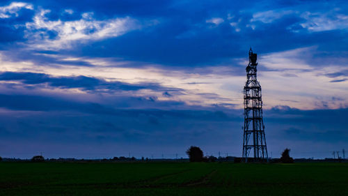 Silhouette tower on field against sky at sunset