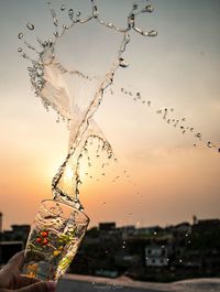 Close-up of glass splashing water against sky during sunset
