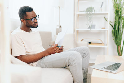 Side view of man using mobile phone while sitting on sofa at home