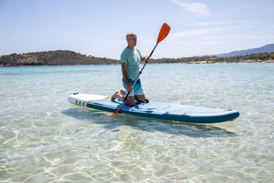 Sup surfing.beautiful view of the sea with a mature man kneeling on a board with paddle in the water