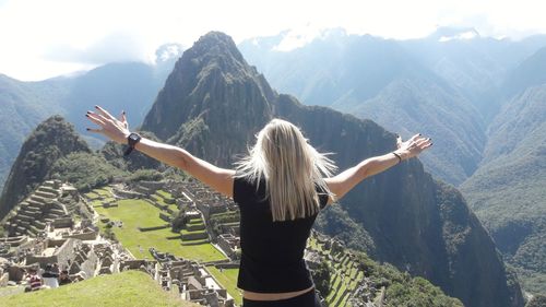 Rear view of woman with arms outstretched standing against mountain