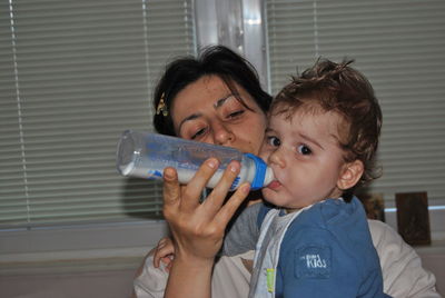 Mother feeding milk to cute son from bottle at home