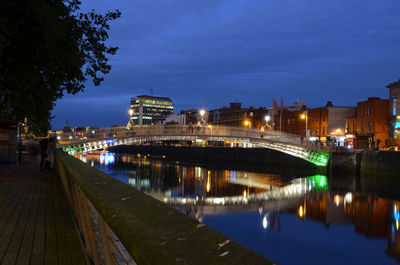 Illuminated bridge over river by buildings against sky at night