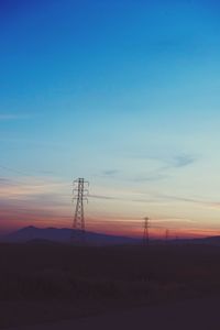 Silhouette electricity pylons on landscape against blue sky