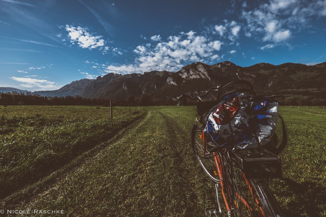 transportation, sky, landscape, field, grass, road, land vehicle, mountain, bicycle, cloud - sky, tranquil scene, tranquility, rural scene, mode of transport, grassy, country road, nature, the way forward, scenics, beauty in nature