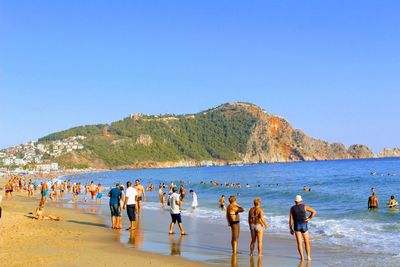 People on beach against clear blue sky