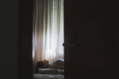 Woman lying on bed at home seen through open door