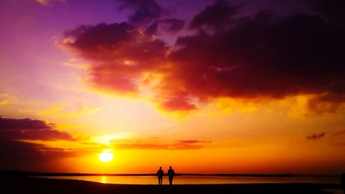 Silhouette people on beach against sky during sunset