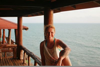 Portrait of smiling woman sitting on railing by sea