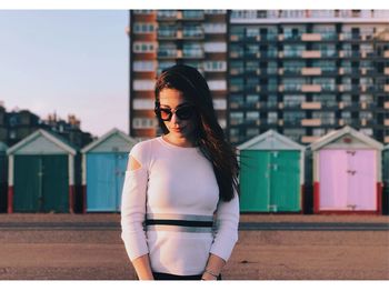 Young woman standing against huts at beach in city