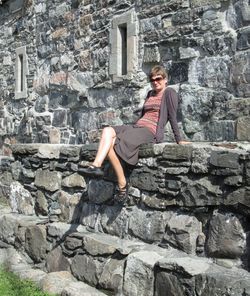 Full length of woman sitting on rock against wall