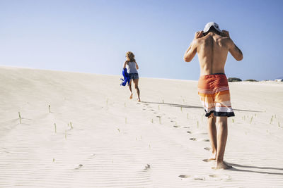 Rear view of friends moving up on sand dune against sky