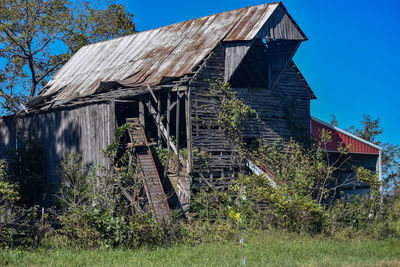 Abandoned house amidst trees on field against sky