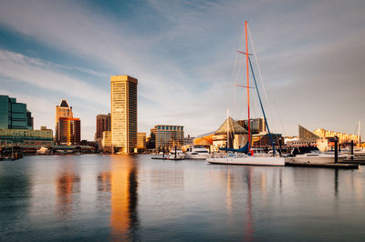 Sailboats moored on sea by buildings against sky