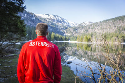 Rear view of man looking at lake against mountain