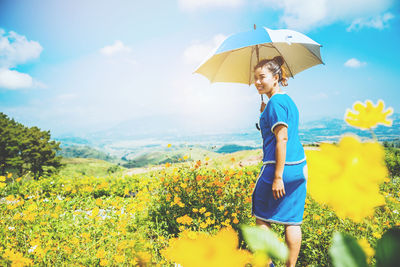 Woman standing by yellow flowers on field against sky