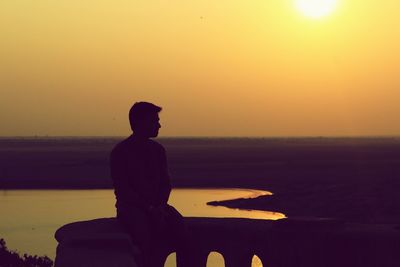 Silhouette of man sitting by sea during sunset