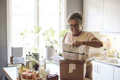 Mature woman with disability opening package in kitchen at home