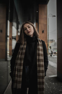 Portrait of young woman in warm clothing standing by building