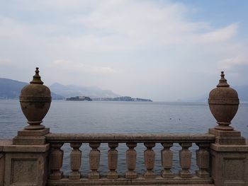 Railing by sea against cloudy sky