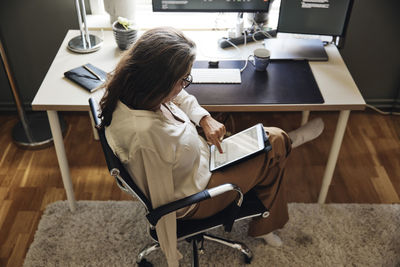 High angle view of businesswoman using tablet pc while sitting on chair at home office