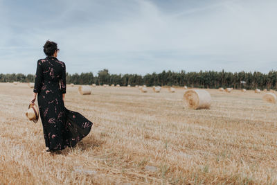 Rear view of woman by hay bales on field