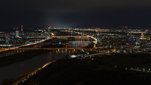 Illuminated cityscape by river against sky at night