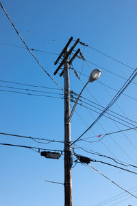 Low angle view of electricity pylon against clear blue sky