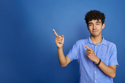 Portrait of smiling young woman gesturing while standing against blue background