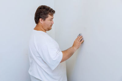 Side view of man standing against white wall