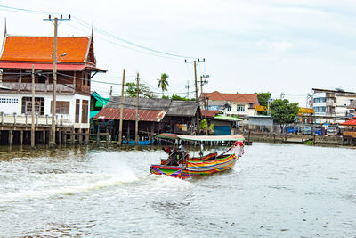 Boats in river by buildings against sky