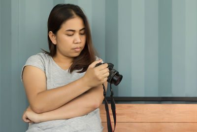 Woman photographing while sitting on bench against wall