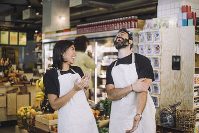 Cheerful multiracial male and female retail clerks wearing aprons standing at grocery store