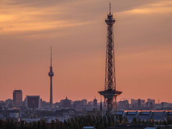 Communications tower in city against sky during sunset