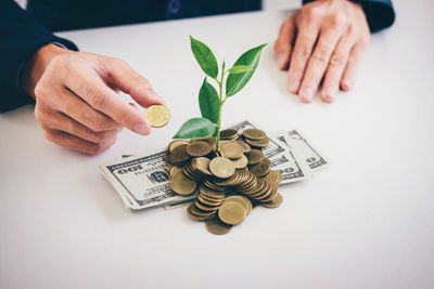 Close-up of businessman holding coin with plant growing amidst currency