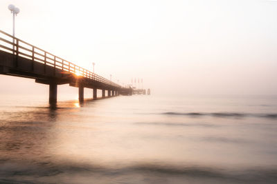 Bridge over sea against sky during sunset