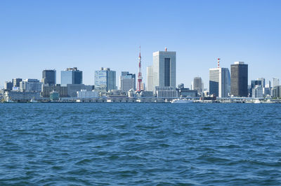 Sea by modern buildings against clear blue sky