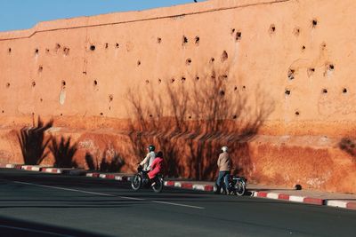 People on motorcycles on street against old wall