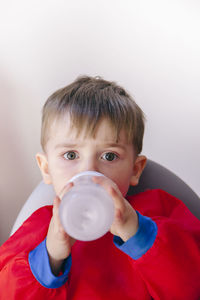 Portrait of cute boy drinking milk against wall