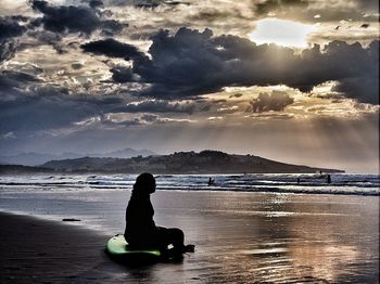 Silhouette man relaxing on beach against sky