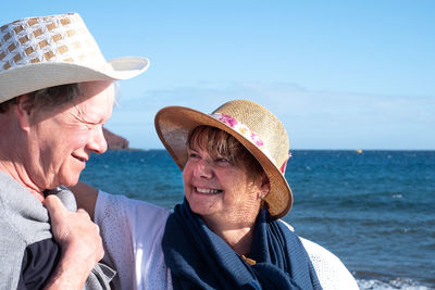 Smiling senior couple standing at beach against blue sky