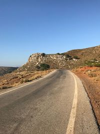 Road leading towards mountain against clear blue sky