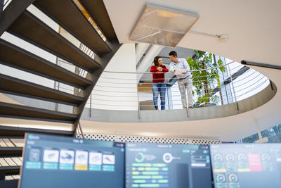 Colleagues talking with each other leaning on banister at office