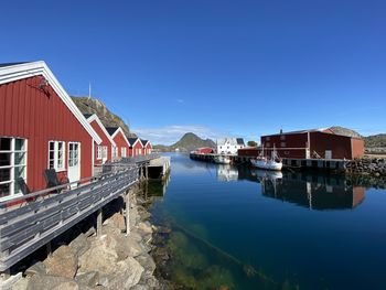 Houses by river and buildings against blue sky